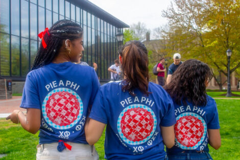 Three women are wearing blue and red shirts with a pie emblem. Their backs are toward the camera.